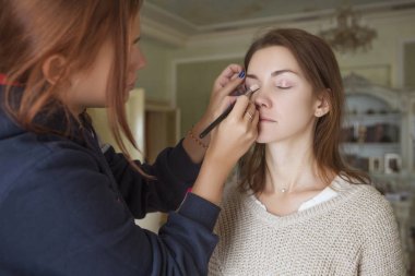 Esmer makyaj sanatçısı kadın beyaz bir esmer gelin, onu düğün photosession veya bir tarih için hazırlama için makyaj uygulanması