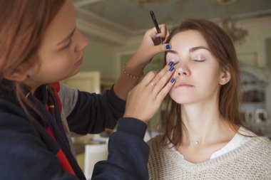 Esmer makyaj sanatçısı kadın beyaz bir esmer gelin, onu düğün photosession veya bir tarih için hazırlama için makyaj uygulanması