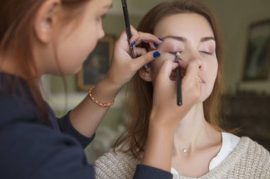 Esmer makyaj sanatçısı kadın beyaz bir esmer gelin, onu düğün photosession veya bir tarih için hazırlama için makyaj uygulanması