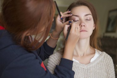 Esmer makyaj sanatçısı kadın beyaz bir esmer gelin, onu düğün photosession veya bir tarih için hazırlama için makyaj uygulanması