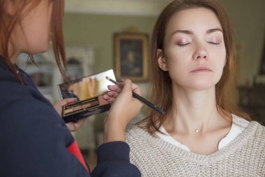 Esmer makyaj sanatçısı kadın beyaz bir esmer gelin, onu düğün photosession veya bir tarih için hazırlama için makyaj uygulanması