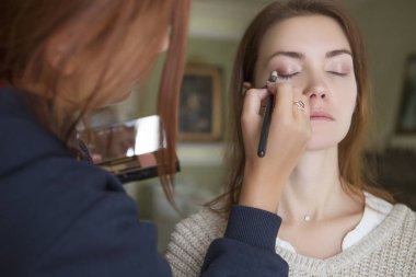 Esmer makyaj sanatçısı kadın beyaz bir esmer gelin, onu düğün photosession veya bir tarih için hazırlama için makyaj uygulanması