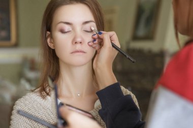 Esmer makyaj sanatçısı kadın beyaz bir esmer gelin, onu düğün photosession veya bir tarih için hazırlama için makyaj uygulanması
