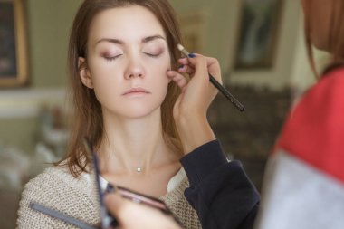 Esmer makyaj sanatçısı kadın beyaz bir esmer gelin, onu düğün photosession veya bir tarih için hazırlama için makyaj uygulanması