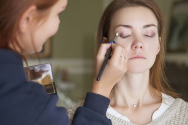 Esmer makyaj sanatçısı kadın beyaz bir esmer gelin, onu düğün photosession veya bir tarih için hazırlama için makyaj uygulanması