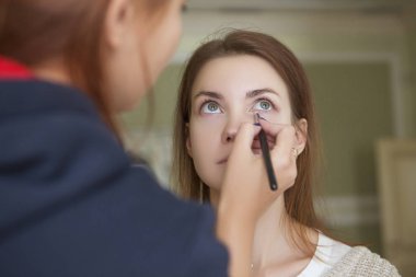 Esmer makyaj sanatçısı kadın beyaz bir esmer gelin, onu düğün photosession veya bir tarih için hazırlama için makyaj uygulanması