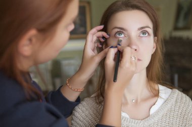 Esmer makyaj sanatçısı kadın beyaz bir esmer gelin, onu düğün photosession veya bir tarih için hazırlama için makyaj uygulanması