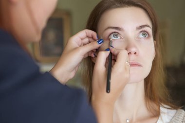 Esmer makyaj sanatçısı kadın beyaz bir esmer gelin, onu düğün photosession veya bir tarih için hazırlama için makyaj uygulanması