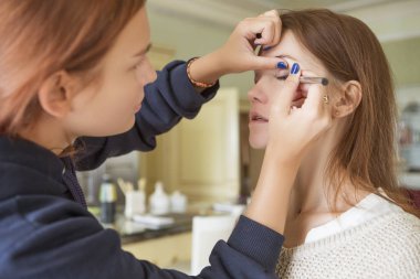 Esmer makyaj sanatçısı kadın beyaz bir esmer gelin, onu düğün photosession veya bir tarih için hazırlama için makyaj uygulanması