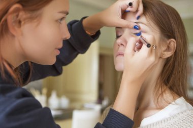 Esmer makyaj sanatçısı kadın beyaz bir esmer gelin, onu düğün photosession veya bir tarih için hazırlama için makyaj uygulanması