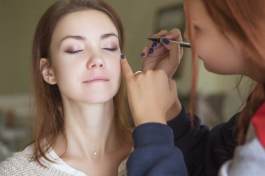 Esmer makyaj sanatçısı kadın beyaz bir esmer gelin, onu düğün photosession veya bir tarih için hazırlama için makyaj uygulanması