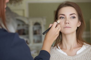 Esmer makyaj sanatçısı kadın beyaz bir esmer gelin, onu düğün photosession veya bir tarih için hazırlama için makyaj uygulanması
