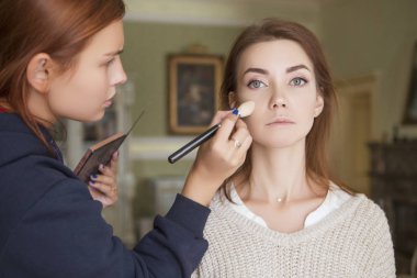 Esmer makyaj sanatçısı kadın beyaz bir esmer gelin, onu düğün photosession veya bir tarih için hazırlama için makyaj uygulanması