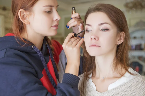 Esmer makyaj sanatçısı kadın beyaz bir esmer gelin, onu düğün photosession veya bir tarih için hazırlama için makyaj uygulanması