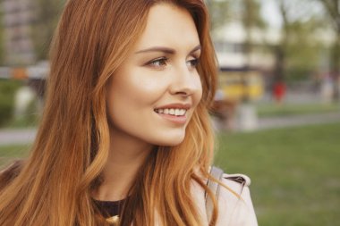 Kızıl saçlı seksi artı bir parkta yürüyen boyutu kadın. Soğuk havada deri ceket giyiyor. Duygusal portre