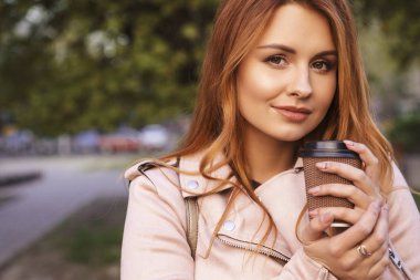 Kızıl saçlı seksi artı bir parkta yürüyen boyutu kadın. Soğuk havada deri ceket giyiyor. 