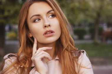 Kızıl saçlı seksi artı bir parkta yürüyen boyutu kadın. Soğuk havada deri ceket giyiyor. Duygusal portre