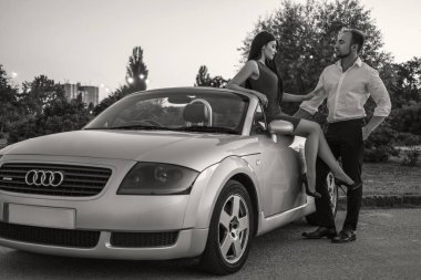 Yaz günü bir tatil araba gezisi erkek ve kadın Muhteşem seksi copule. Lüks gri spor araba. Seksi uygun esmer kadın ve akşam kıyafeti adam. Gece portresi.