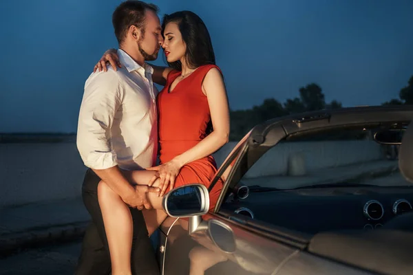 Yaz günü bir tatil araba gezisi erkek ve kadın Muhteşem seksi copule. Lüks gri spor araba. Seksi uygun esmer kadın ve akşam kıyafeti adam. Gece portresi.