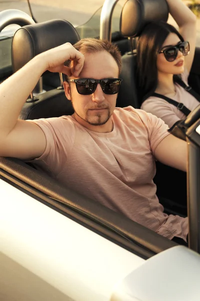 Gorgeous sexy copule of man and woman on a vacation car trip in summer day. Luxury grey sport car. Sexy fit brunette woman and man in casual outfit. Sunset.