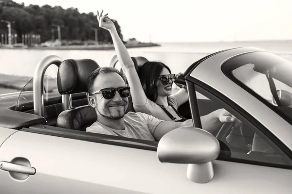 Gorgeous sexy copule of man and woman on a vacation car trip in summer day. Luxury grey sport car. Sexy fit brunette woman and man in casual outfit. Sunset.