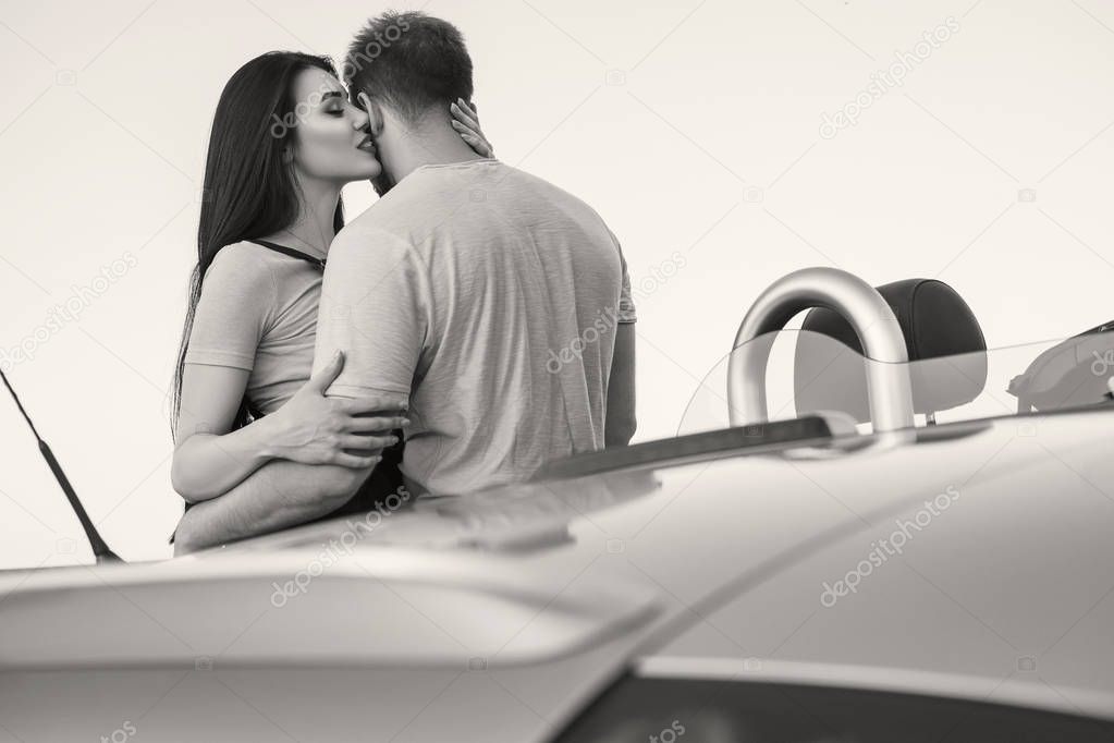 Gorgeous sexy copule of man and woman on a vacation car trip in summer day. Luxury grey sport car. Sexy fit brunette woman and man in casual outfit. Sunset.