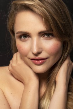 Taze, temiz, sağlıklı, kusursuz bir cildi olan sevimli gülümseyen sarışın beyaz kadın. Çıplak, gün rahat saç modeli ile makyaj. Yüzünde küçük çiller vardı. Siyah arka plan üzerinde portre.