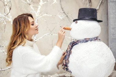 Evin yakınında sevimli artı boyutu kadın, çelenk ve noel süslemeleri kaplı. Beyaz rahat kazak giyiyor. Metin için alan