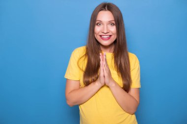 Mavi bir arka plan üzerinde sarı t-shirt poz uzun saçlı sevimli esmer kadın. Duygusal portre. Kusursuz beyaz dişleri ile mutlu bir şekilde gülümsüyor.