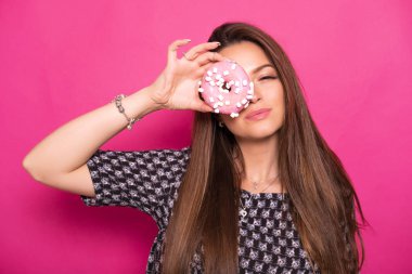 Pembe bir arka plan üzerinde uzun esmer saçlı seksi model. Duygusal portre. Çörek yiyor.