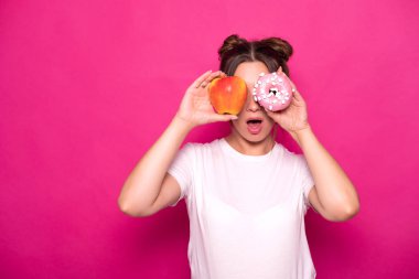Seksi model pembe bir arka plan üzerinde beyaz tişört içinde şık saç modeli ile. Duygusal portre. O şok, hayret, iyi ve kötü gıda arasında seçmek için bağlama: elma veya çörek?