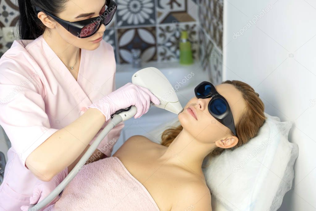 Woman doctor cosmetologist removing hair from a woman client body using laser epilator. They in a spa center.