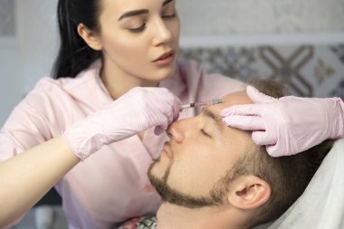 Güzellik closeup ana yapıyor enjeksiyon In genç erkek hasta Face. Güzellik yordamı kullanarak dolgu enjeksiyonları almak adam. Kozmetik ve Güzellik yüz enjeksiyon kavramı