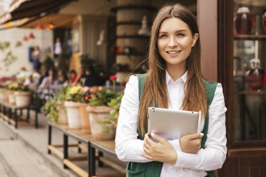Güzel esmer iş kadını beyaz bluz ve yeşil ceket elleri açık havada bir tablet üzerinde çalışıyor. Avrupa şehirde serbest meslek. Metin için yer.