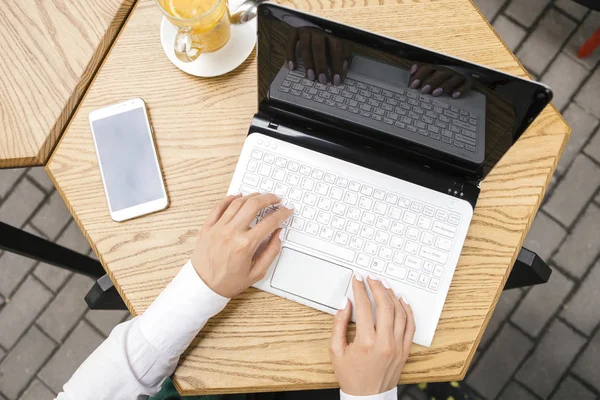 Brunette business woman working as a freelancer from a cafe in summer terrace. She drinks tea and use gadgets as laptop and tablet and phone for her work. Space for text. Top view from above.