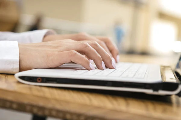 Woman typing on a laptop keyboard in a warm sunny day outdoors, sitting at the cafe table. Space for text.