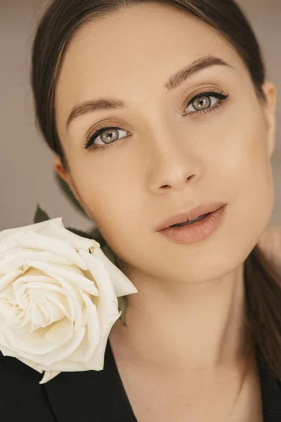 Sexy fit brunette caucasian woman in dress and jacket at home. Pretty flawless face. She holds flower.