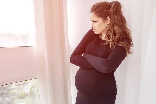 Wanita cantik berambut cokelat hamil di rumah dengan gaun hitam — Stok Foto