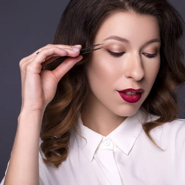 Brunette woman beautician on a neutral background. She holds bea