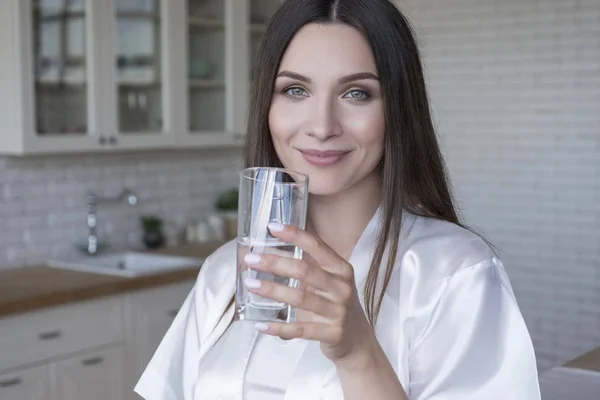 Mooie pasvorm brunette vrouw thuis in pyjama. Ze drinkt water — Stockfoto