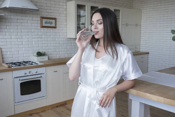 Mooie pasvorm brunette vrouw thuis in pyjama. Ze drinkt water — Stockfoto
