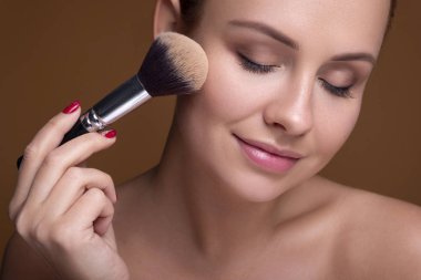 Kafkas esmer kadın bir fırçayla elmacık kemiğine allık sürüyor.