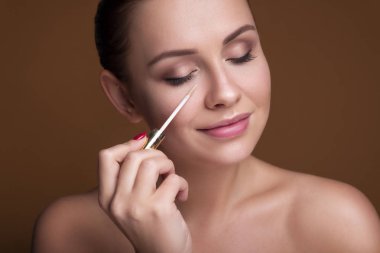 Esmer beyaz kadın gözlerinin altına kapatıcı sürmüş. Hatalar