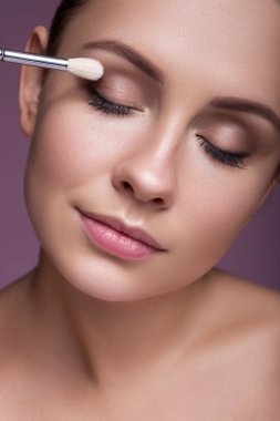 Esmer, beyaz bir kadın bir Bru ile göz farı sürüyor.