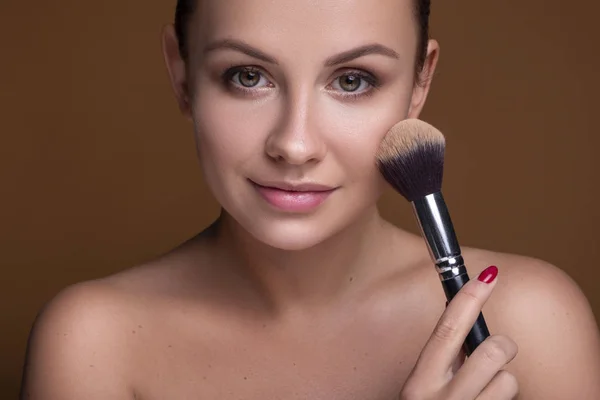 Caucasian brunette woman apply blush on a cheekbone with a brush