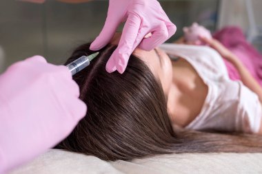 Kozmetik doktoru kliniğinde bir kadına iğne yapıyor. Pembe parıltı ve maske takıyor ve şırıngayı iğneyle tutuyor..