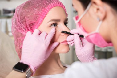 Kozmetik doktoru klinikteki kadın bir müşteriye iğne yapıyor. Maske ve eldiven takıyor..