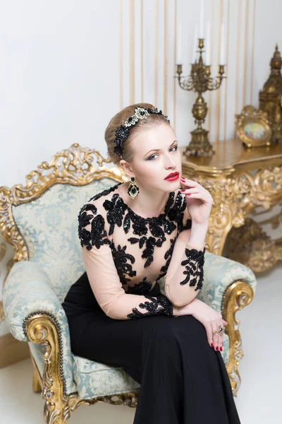 ゴージャスな豪華なドレスでレトロな椅子に座って美しいブロンドの王室の女性 屋内だ コピースペース — ストック写真