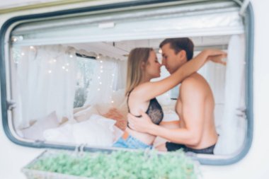 Odaklanmamış, bulanık bokeh görüntüsü. Genç aşıklar birbirlerini okşarlar. Birbirlerine sevgiyle sarılıp öpüşüyorlar. Pencereden evde yatakta çekilmiş bir yaz portresi. Metin için alanı olan arkaplan.