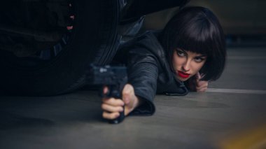 Güzel esmer, seksi ajan (katil ya da polis) Deri ceketli ve kot pantolonlu bir kadın, birinin peşinden koşuyor, onu park yerinde yakalamak için..